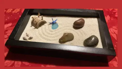 Black lacquered box with sand and rocks with rake marks with a red background 