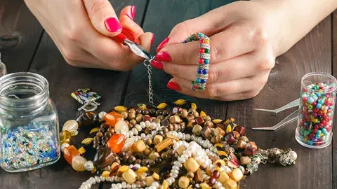 Hands with painted red nails using tools and beads to make a jewelry piece.