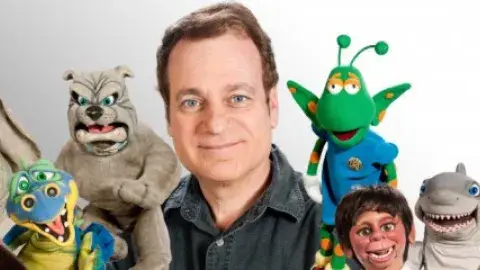 A smiling man is surrounded by colorful puppets