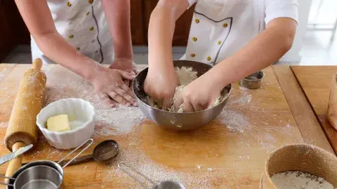 Two children mixing ingredients in a bowl on a kitchen counter with their hands