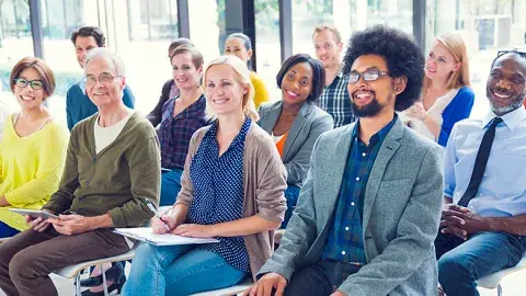 A group of adult learners smiling and practicing English pronunciation and everyday idioms together in a library classroom.