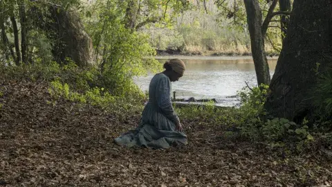 A woman sitting on her knees near a river 