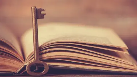An old key leans on the spine of an open book