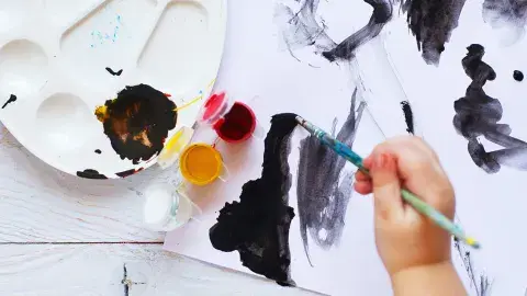 a young child's hand is using a brush to paint with black paint