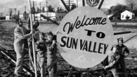 black and white photo of people around sign that reads welcome to sun valley