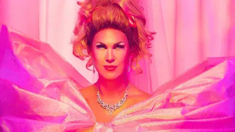 Head and shoulders view of Drag Performer Pickle in a pink gown, with a jeweled necklace and earrings, big hair, and full make-up.