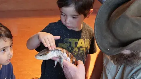 A child gingerly touches a reptile