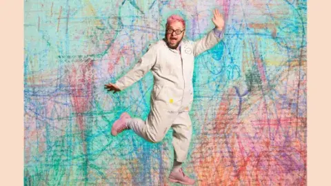 Ricky Rainbow Board jumping in front of a colorful background. 