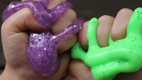 hands squishing purple glittery and green slime