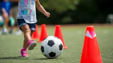 A child kicking a soccer ball between orange cones