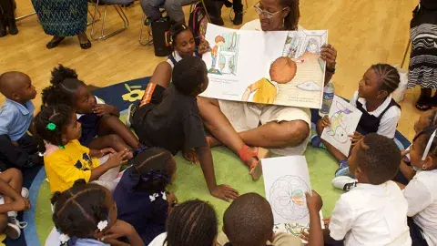 woman reading an oversized book to a group of children