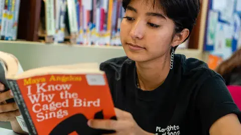 Teen girl holding up a book and reading.