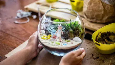 Two hands holding a glass terrarium with a beach scene inside