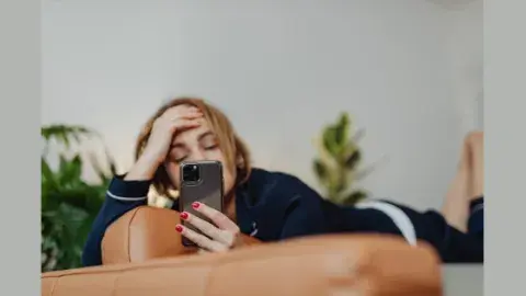 young person laying on a couch with a smartphone obscuring their face