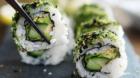 a plate of vegan sushi with one sushi grasped by black chopsticks