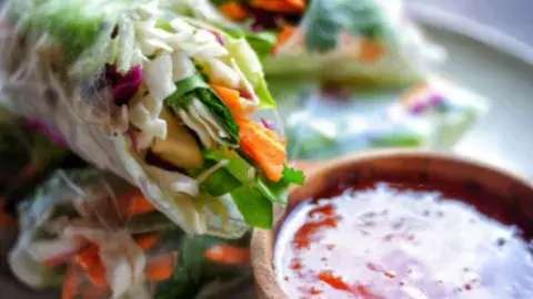 Image of two spring rolls with fresh veggies and a red dipping sauce