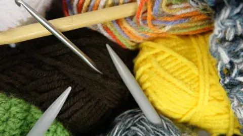 A collection of multicolored skeins of wool and knitting needles.