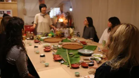 People seated at a table watching a woman do a demonstration