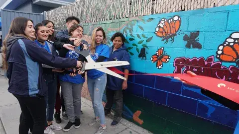 teens with giant scissors cutting a ribbon by a painted mural