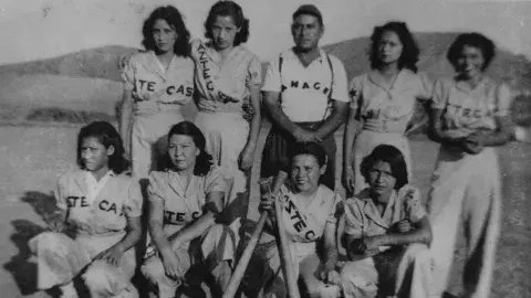 Group portrait of the Aztecas, a girls’ baseball team based in Pacoima, with their manager