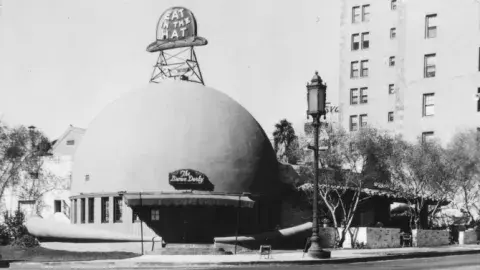 Exterior of a dome-shaped building with signage that reads "Eat in the hat" and "The Brown Derby"