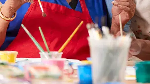 colorful paints and paintbrushes on table with people in background