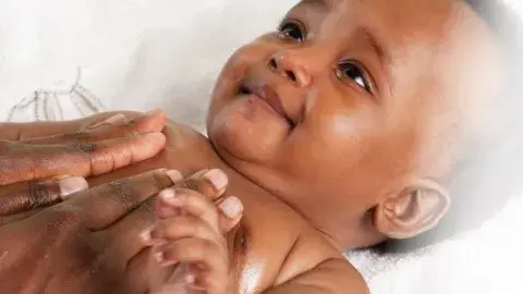 a baby looks up as adult hands massage the baby
