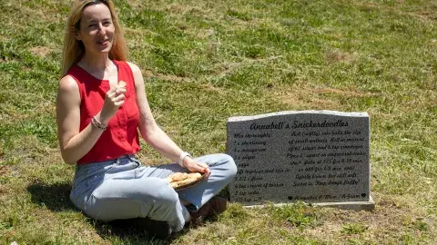 woman sitting near a gravestone holding a cookie