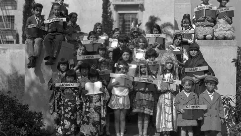 Children dressed in various costumes holding signs with various languages.