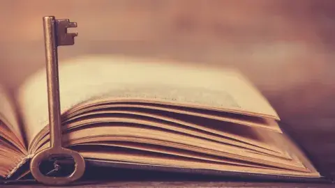An open book with a skeleton style key before it.