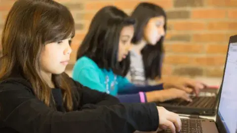 Three students sitting, using laptop computers.