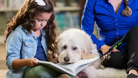 An adult and child reading with a therapy dog