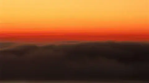 Sky during sunrise featuring a gradient of orange and dark clouds