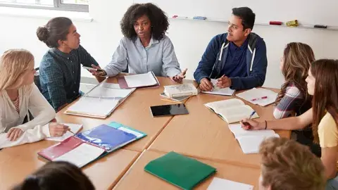 Eight students sit in chairs around a conference table.