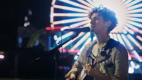 Person singing at a microphone in front of a lit-up ferris wheel.
