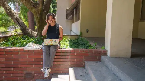 person sits on edge of planter with laptop and headphones