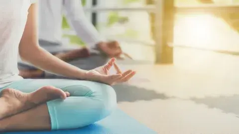 Two people seated on a floor in a yoga position with sunlight shining on them from the side.