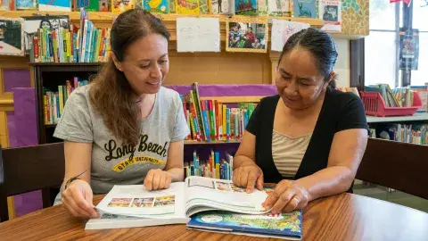 A tutor and adult learner are looking through a workbook.