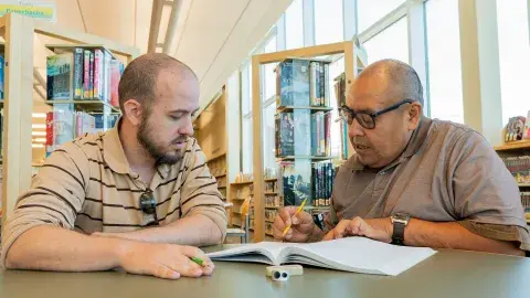 A tutor and adult learner are looking through a workbook.