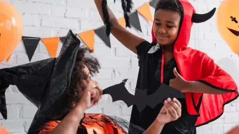 A child dressed as a witch and a child dressed as a devil hang Halloween decorations.