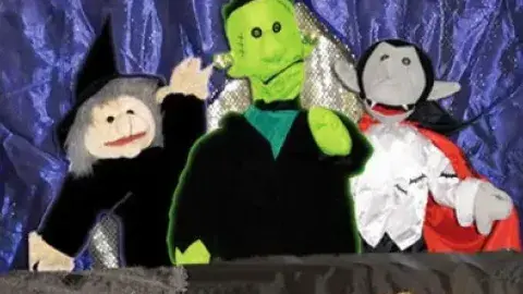 Monster puppets smile in front of sparkly purple background. 