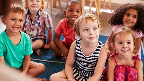 Group of young kids sit on floor rugs listening to a story