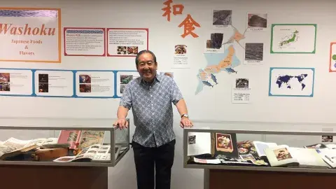 Samuel H. Yamashita stands next to glass cases at exhibit with the title, "Washoku: Japanese Foods and Flavors"