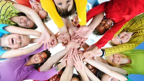 A diverse group of smiling people put their hands together in a circle