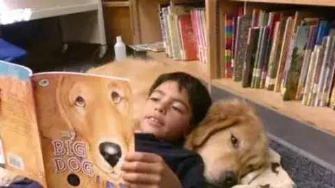 Child resting against a Golden Retriever reading.