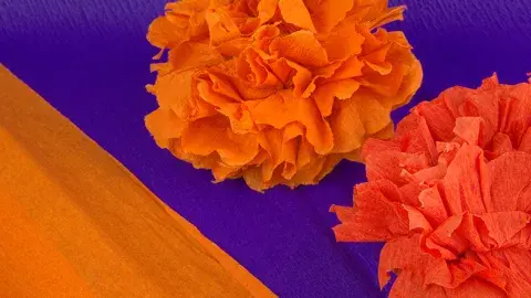 Close up of paper marigolds against a deep purple background.