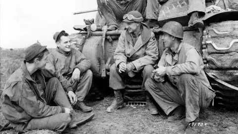 Ernie Pyle sits alongside soldiers