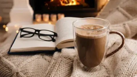 An open book with a cup of hot chocolate next to it 