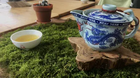 A cup of tea on the left and a blue and white tea pot sitting on a wood log on the right