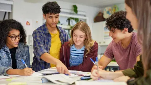 A group of students studying and doing homework around a table together. 